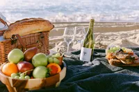 Wicker picnic basket with bread, fruit, wine, and charcuterie set on the sand at sunset
