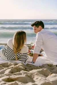 Couple sharing wine on a beach blanket at sunset in Monterey