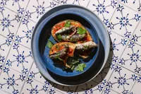 Pan con tomate topped with whole Natural Catch sardines and parsley on hand-painted blue and white tile