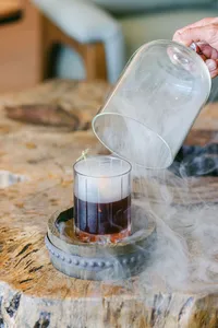 Smoked cocktail revealed under a glass cloche at the bar