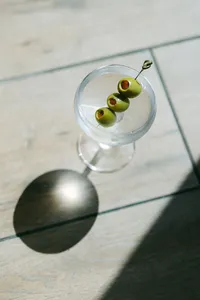 Overhead of a martini with skewered olives on a sunlit table