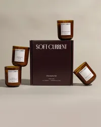 The Soft Current Discovery Set box surrounded by four mini candles in amber glass, stacked and tipped for a playful composition. Candle product photography by Chelsea Loren.