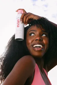 Close frame of a model applying Evian Glow facial mist to her hair, laughing