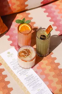 Three cocktails styled with a pool bar menu on a patterned textile