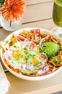 Chilaquiles with fried eggs, avocado, radish, and pickled onion beside green juice and an orange dahlia at Adelaide, hotel restaurant photography