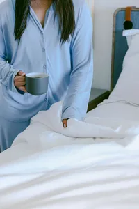 Guest in pajamas with morning coffee beside a bed in an oceanfront guest room
