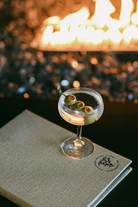 Martini resting on a linen menu beside an open fire