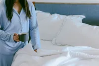 Guest in pajamas with morning coffee beside a bed in an oceanfront guest room