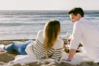 Couple sharing wine and small bites on a blanket above the surf