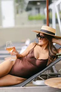 Guest in a straw boater hat and brown swimsuit lounging poolside with a glass of rosé at L’Auberge Del Mar, luxury resort pool photography