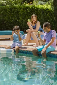 Three kids with ice cream on the edge of the pool in summer