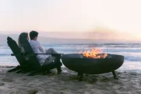 Couple in Adirondack chairs beside a beach firepit at sunset in Monterey