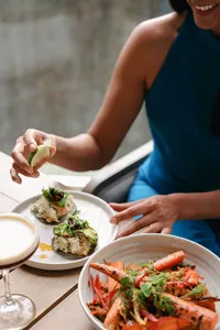 Guest squeezing lime over small plates at Adelaide, with a bowl of prawns and an espresso martini on the table, resort dining photography