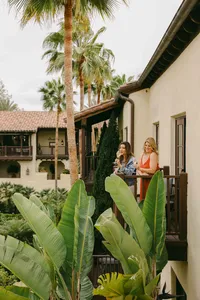 Two guests talking on a guest room balcony above the palms