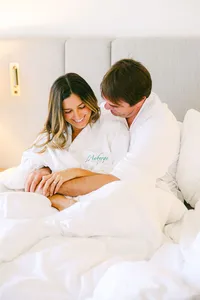 Couple cuddled up in L’Auberge Del Mar robes in a bright guest room, a romantic getaway moment for a luxury hotel campaign