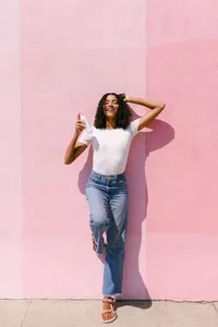 Full-length lifestyle frame against a pink stucco wall, beauty campaign photography