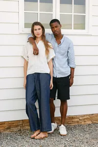 Two models in linen against white horizontal siding, seasonal lookbook frame