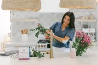 Woman arranging flowers in a bright kitchen wearing a HonestMed lidocaine patch on her arm, with product packaging staged on the counter