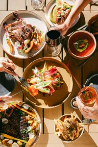 Overhead of a shared table at Adelaide with steak, prawns, crudo, fries, red wine, and cocktails, luxury hotel restaurant photography