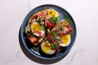Niçoise-style toast with Natural Catch yellowfin tuna, jammy egg, tomato, pickled red onion, and dill on a blue plate