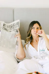 Guest in an L’Auberge Del Mar robe reading the newspaper in bed during a slow morning in a guest room, luxury hotel room photography