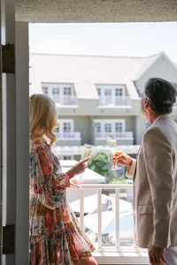 Couple toasting champagne on a guest room balcony overlooking the rooftops and pool umbrellas of L’Auberge Del Mar, luxury hotel lifestyle photography