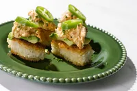 Crispy rice topped with Natural Catch spicy chili tuna, avocado, and jalapeño on a green scalloped plate