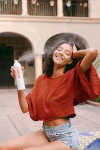 Model spraying Evian facial mist mid-motion in a Spanish-style courtyard