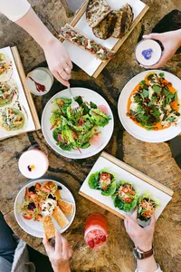 Overhead of a shared table with salads, lettuce wraps, and toasts on a live-edge wood surface
