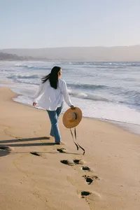 Guest walking the shoreline with a straw hat, footprints in the wet sand