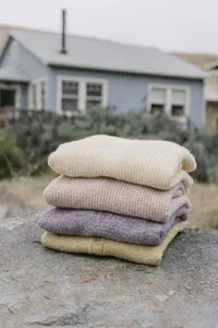 Stack of folded AW26 sweaters in cream, blush, lavender and chartreuse photographed on location