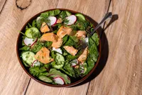Natural Catch teriyaki coho salmon herb salad with radish, cucumber, and dill on a rustic wood table
