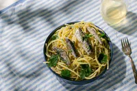 Sardine pasta with lemon, capers, and parsley on blue striped linen with a glass of white wine, made with Natural Catch sardines