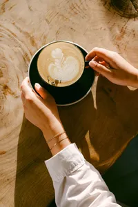 Hands holding a latte with rosetta art over a live-edge wood table