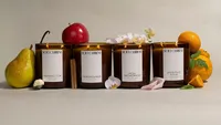The full Soft Current collection lined up with a pear, red apple, white orchids, and fresh oranges, each ingredient matched to its scent. Candle product photography by Chelsea Loren.