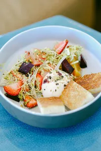 Burrata with strawberries, beets, and grilled bread in a blue ceramic bowl
