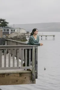 Model in a soft green wrap cardigan leaning on a weathered boardwalk railing