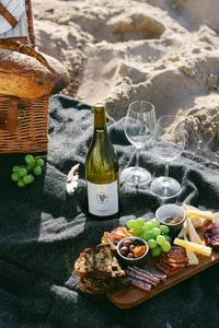 Picnic basket, wine, and a charcuterie board set out on the sand