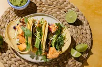 Natural Catch teriyaki coho salmon tacos with slaw, avocado, cilantro, and lime on a woven placemat