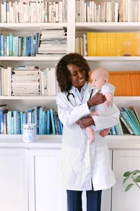 Pediatrician in a white coat holding an infant beside a tin of Kabrita goat milk formula, healthcare brand lifestyle campaign
