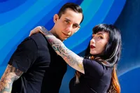 Hugo and Stacy in a dance pose in front of a blue mural, photographed by Dan Sweet in 2025.