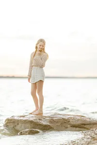 Beautiful soft sunset photo of a girl standing on a rock on the side of a lake as she looks over her shoulder to pose for the photographer.