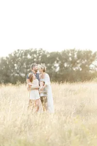 Family of 4 photo of them all standing together in an open grassy park in Dallas as they cold each other and pose for their photographer.