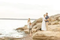 A lake family photo as mom and dad stand together on the rocks while the children are playing in the water.