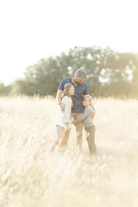 Dad holding his two children close as they stand together in the middle of a grassy field at a Fort Worth park.