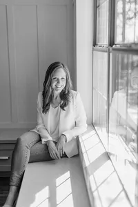 Beautiful black and white professional headshot photo of a Dallas Texas business woman posing by a window smiling at the camera for her branding/headshot session.