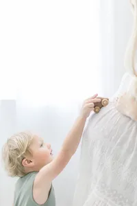 A little boy playing with a wooden toy car on his moms belly for her maternity photos in a Dallas photography studio.