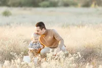 A father kneeling down next to his son in the middle of a Dallas park as he kisses his sons forehead.