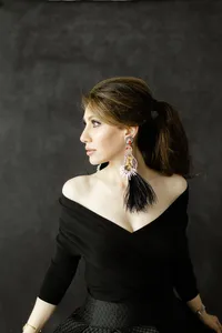 A photo of a woman posing for boudoir photos in a studio as she wears a black off the shoulder gown and looks over her shoulder elegantly.