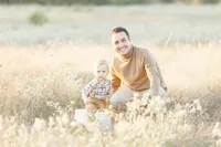 A father posing next to his son at a local Dallas park as they both look and smile at their family photographer.